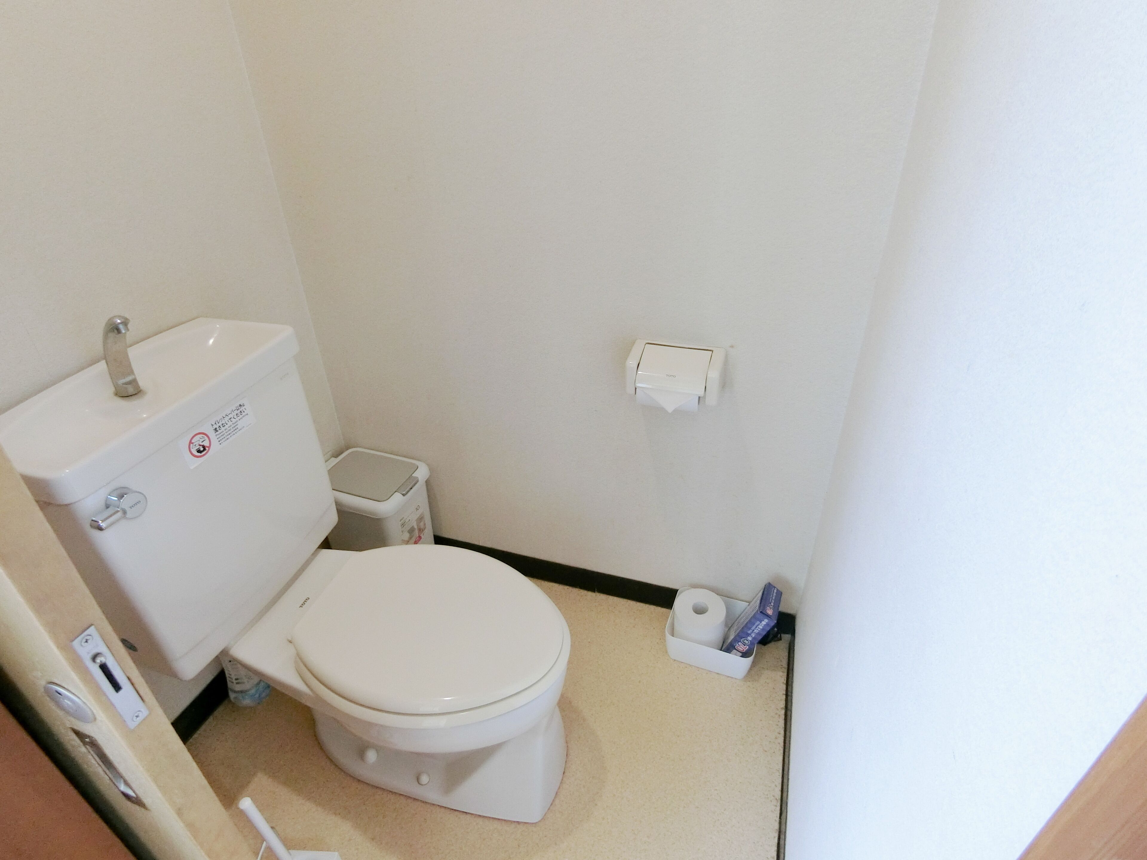 Un baño pequeño y limpio con inodoro, lavamanos y dispensador de papel higiénico.