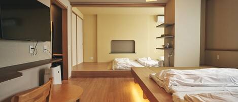A hotel room with a bed, a desk, a chair, a television, and a shelf.