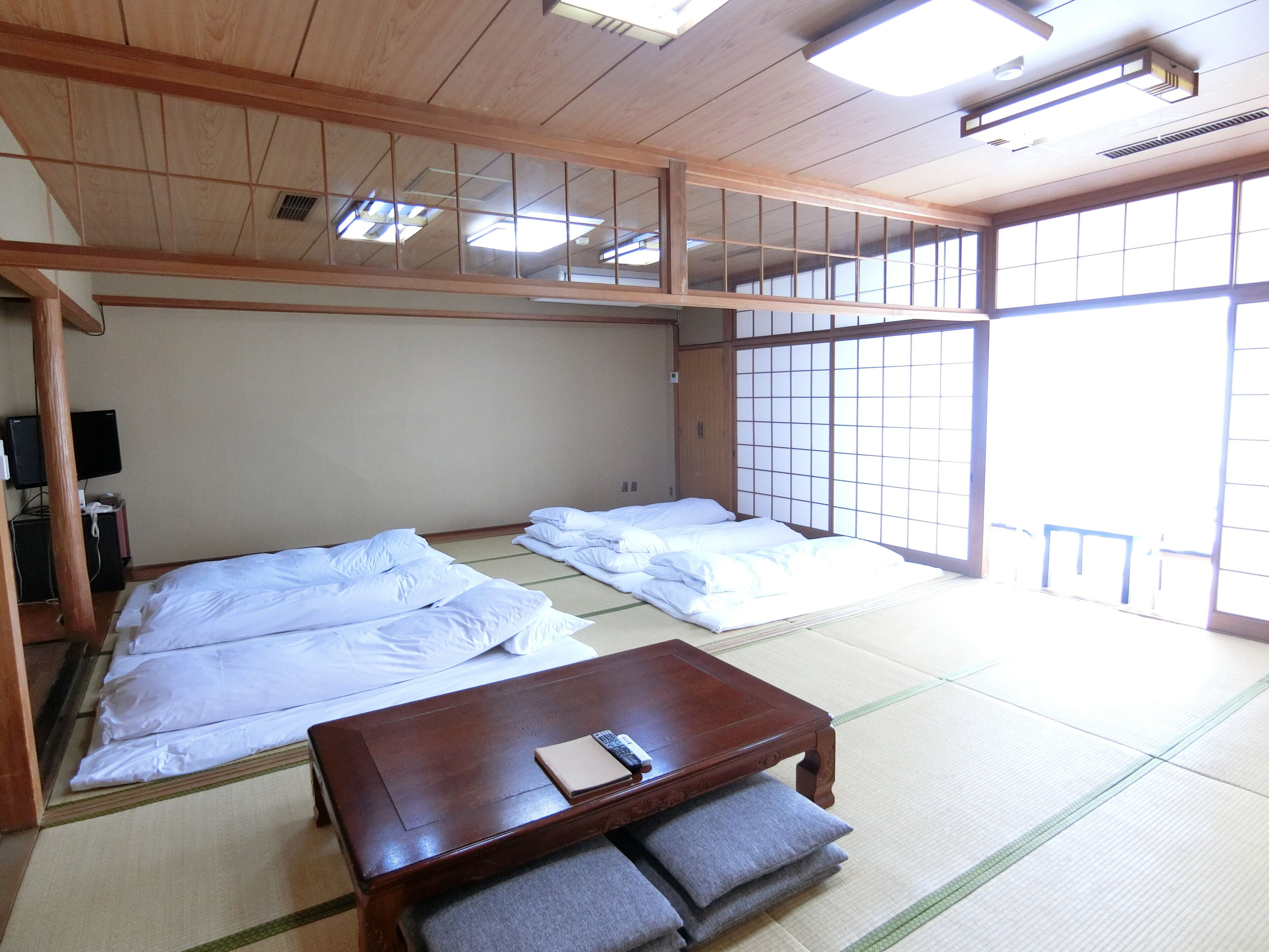 Perinteinen japanilaistyylinen huone, jossa on tatamimatto, kaksi sänkyä, puinen pöytä ja televisio.