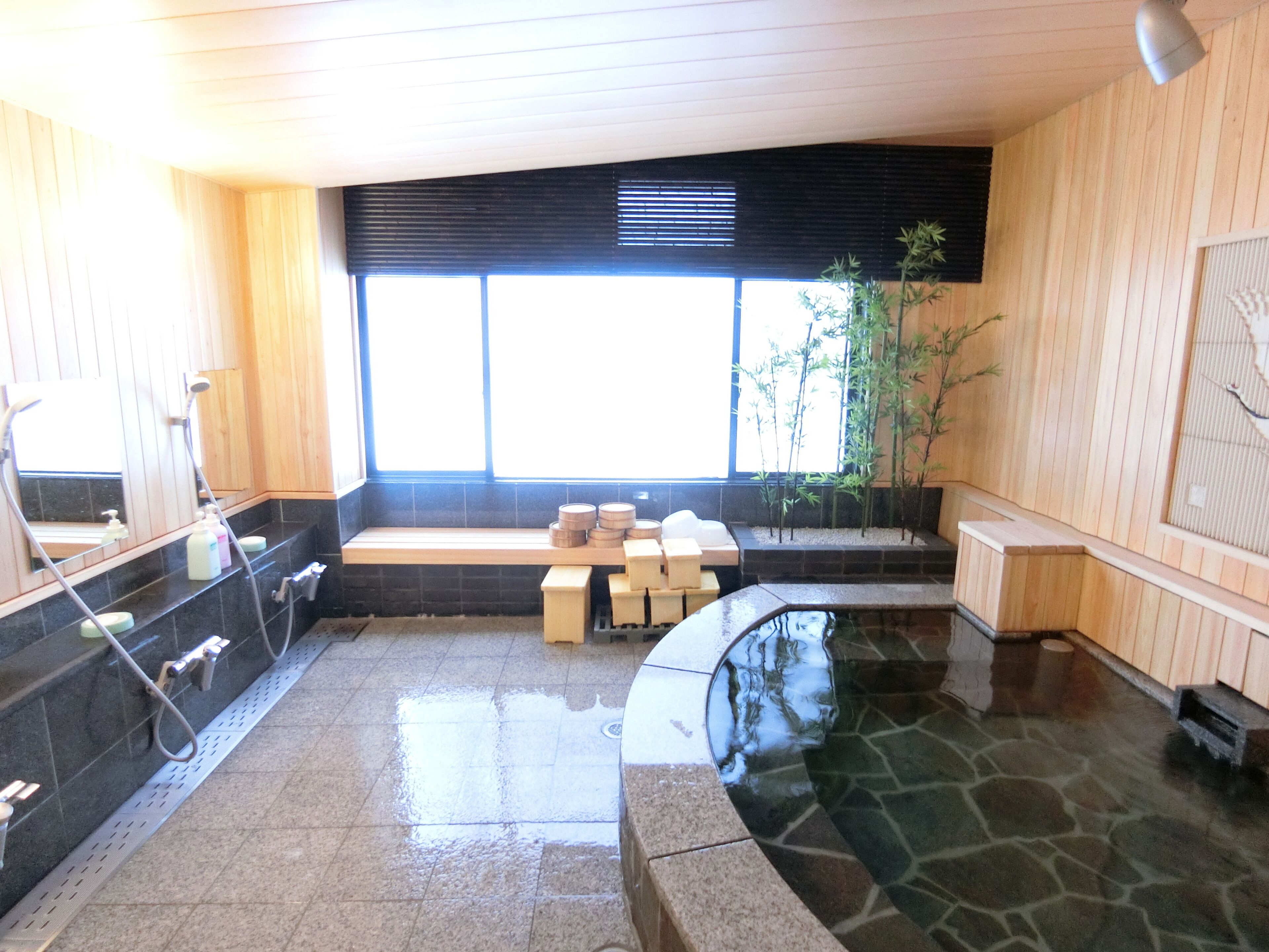 A traditional Japanese onsen with a stone bath, wooden benches, and bamboo plants.