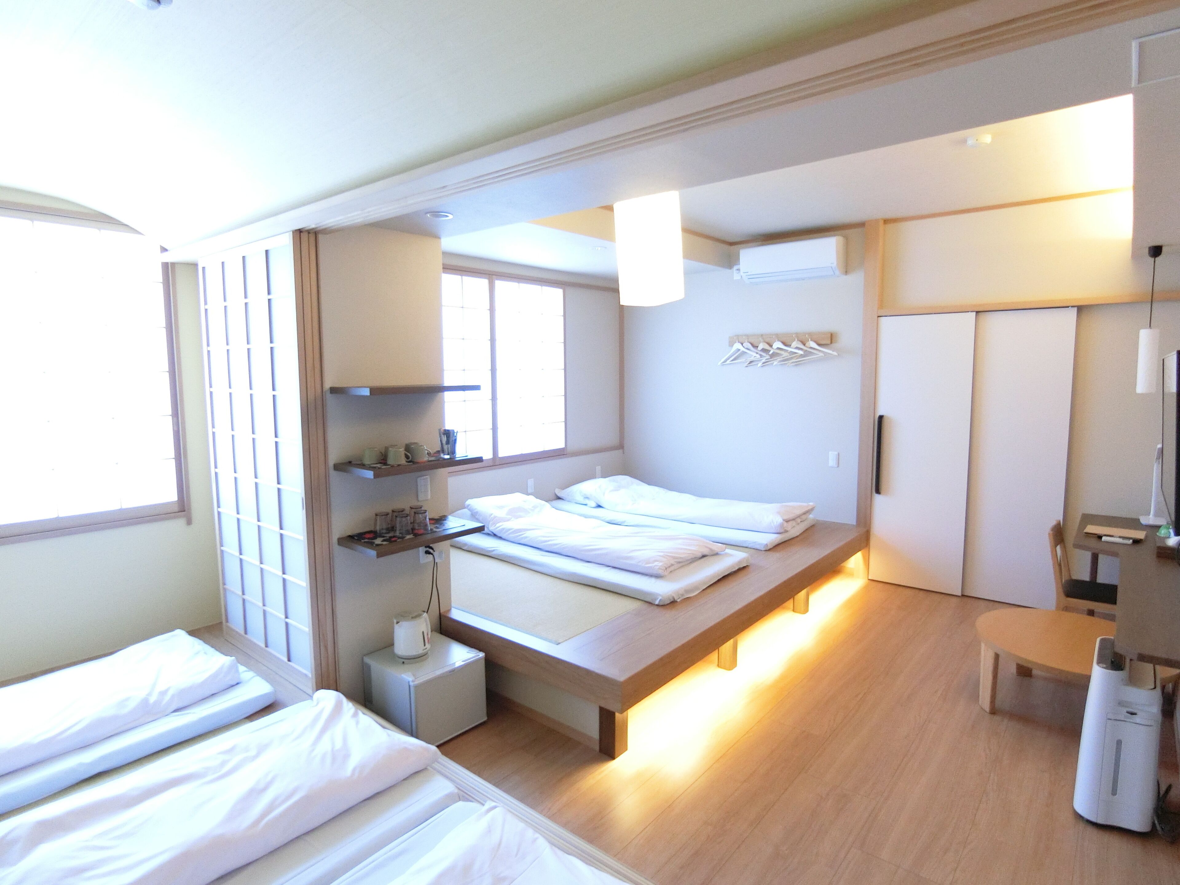 A hotel room with a bed, bedside table, lamp, and a small desk with a chair.