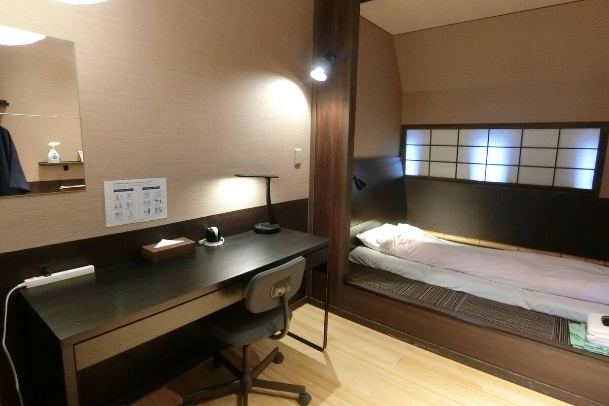 Ein kleines Hotelzimmer mit Schreibtisch, Stuhl und einem Einzelbett.