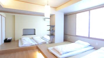 A hotel room with two beds, a small desk, a TV, and a window.