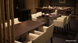 Un restaurante con varias mesas y sillas, separadores de bambú y un ambiente oscuro.