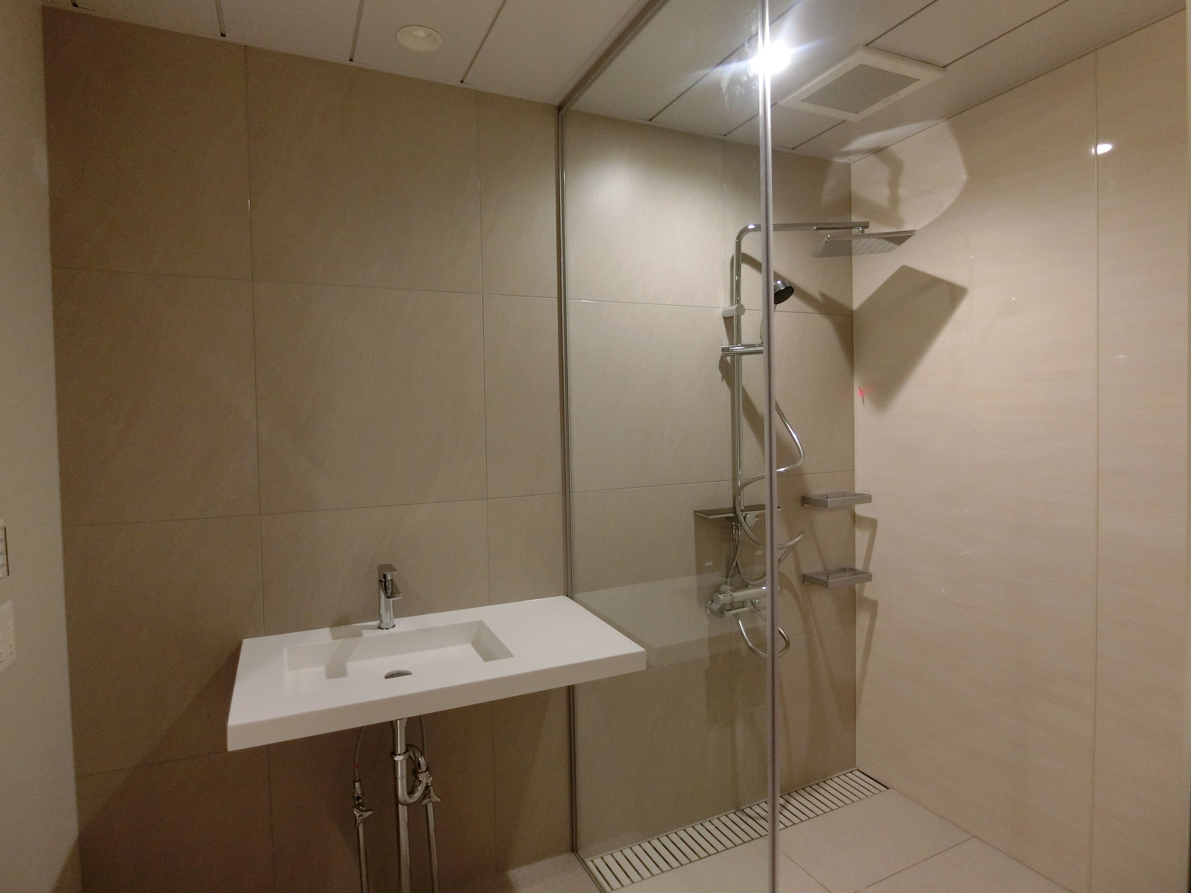 Ein modernes Badezimmer mit einer gläsernen Duschkabine, einem weißen Waschbecken und beige gefliesten Wänden.