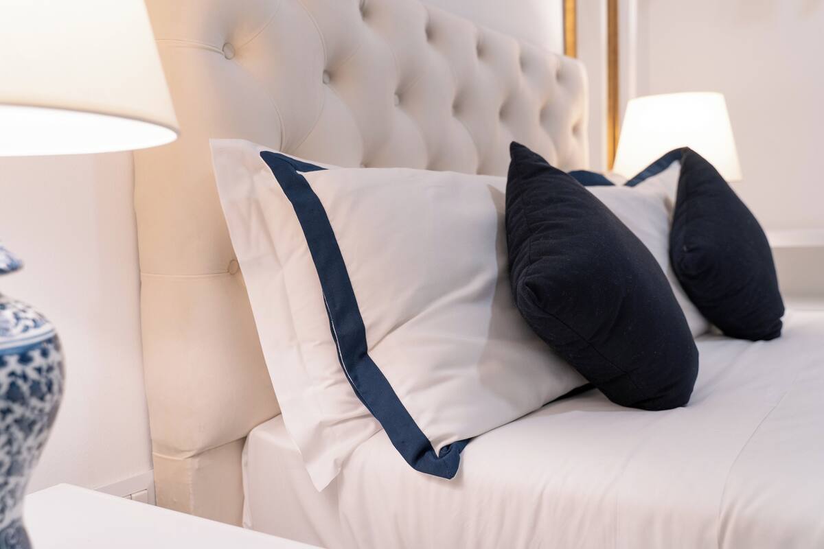 A neatly made bed with white and navy blue pillows, a tufted headboard, and a bedside table with a lamp.