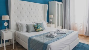 A neatly made bed with a quilted headboard, a bedside table with a lamp, and a wardrobe in a room with blue walls. - La Residenza di Michelangelo (Florence)