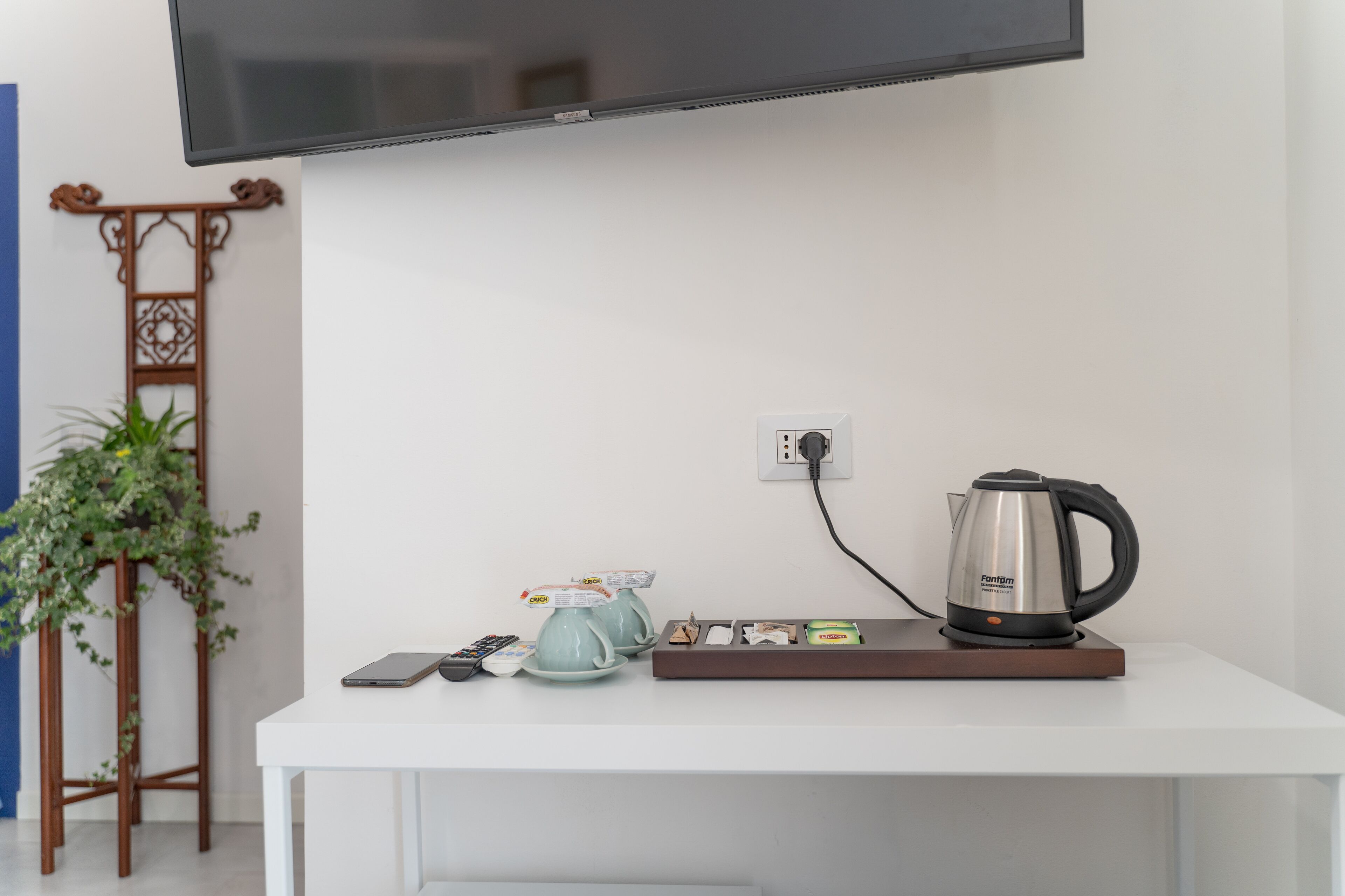 A white desk with a kettle, two teapots, a remote control, and a smartphone.