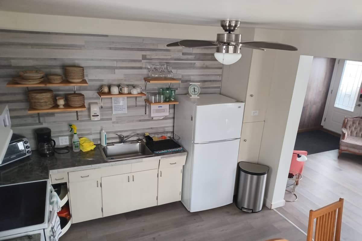 Una cucina compatta con frigorifero integrato, macchina del caffè e lavandino. Sopra il bancone si trovano scaffali in legno con piatti e bicchieri.