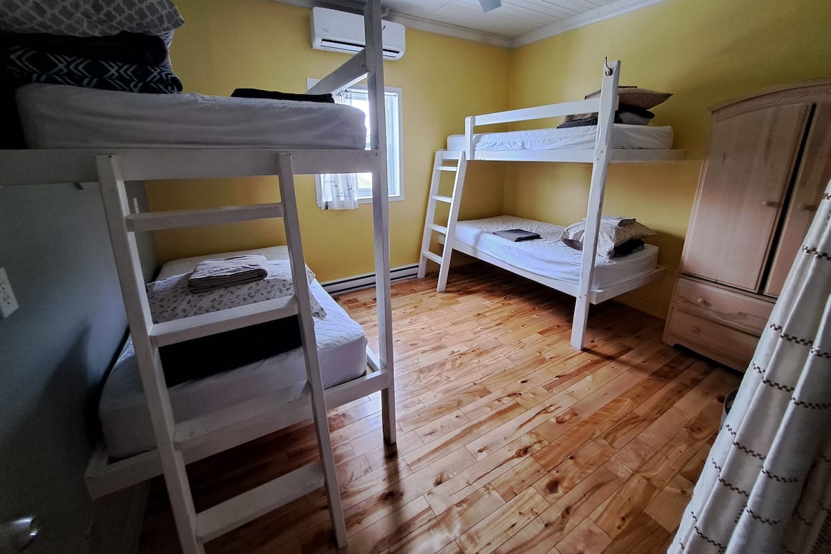 Una camera del dormitorio con letti a castello, pavimento in legno, una ventola a soffitto e un condizionatore d'aria.