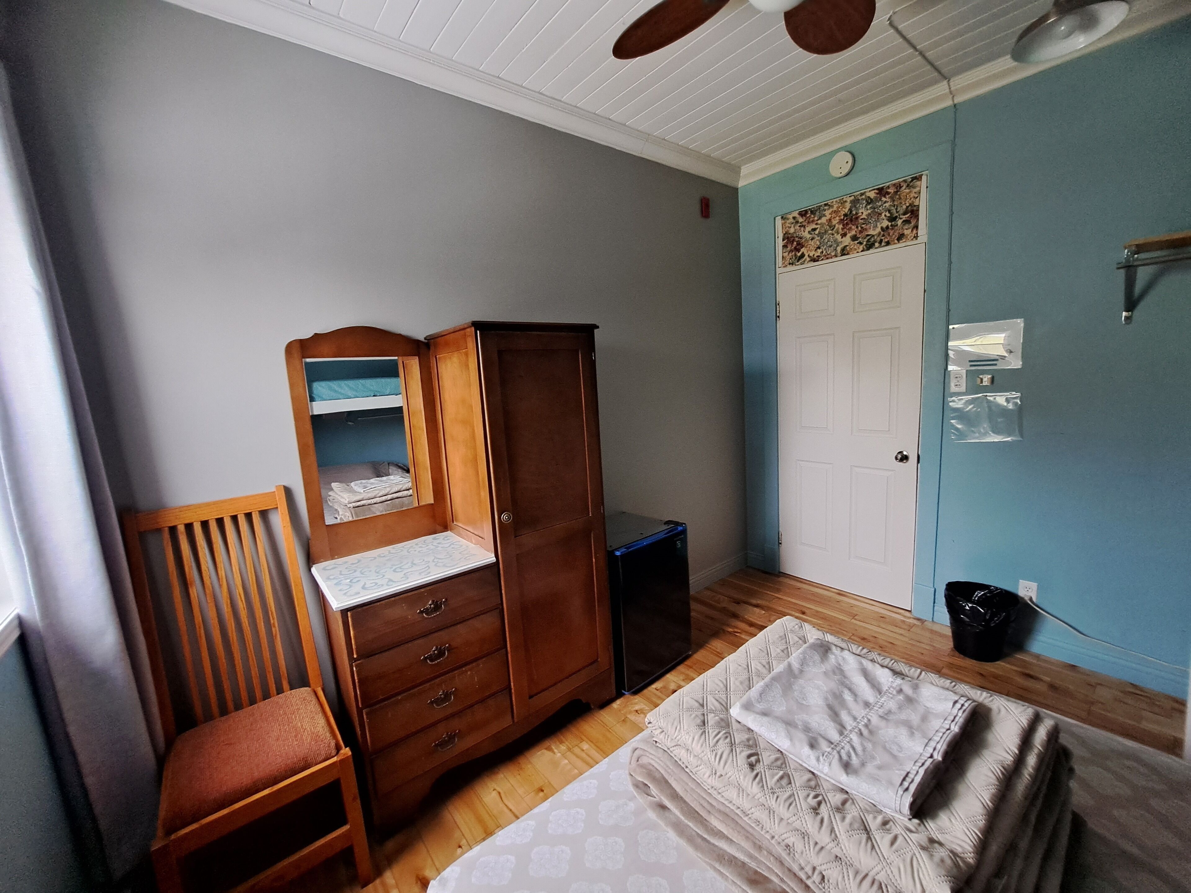 Un dormitorio con un armario de madera, una cama individual, una silla y un ventilador de techo.