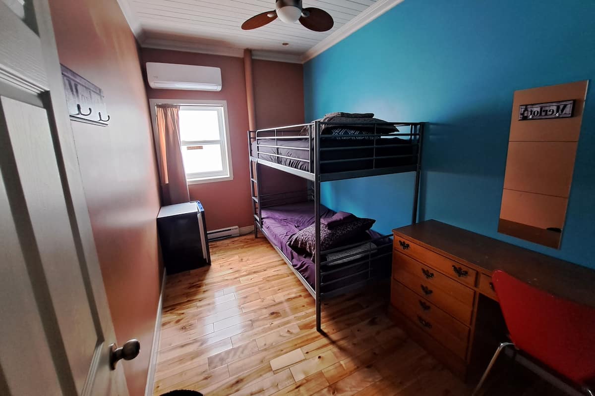 Una camera del dormitorio con letti a castello, una scrivania, una sedia, una ventola a soffitto e una finestra.