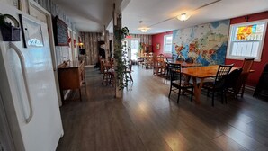 Un restaurante con suelo de madera, una gran mesa de comedor y sillas. Hay un refrigerador a la izquierda.