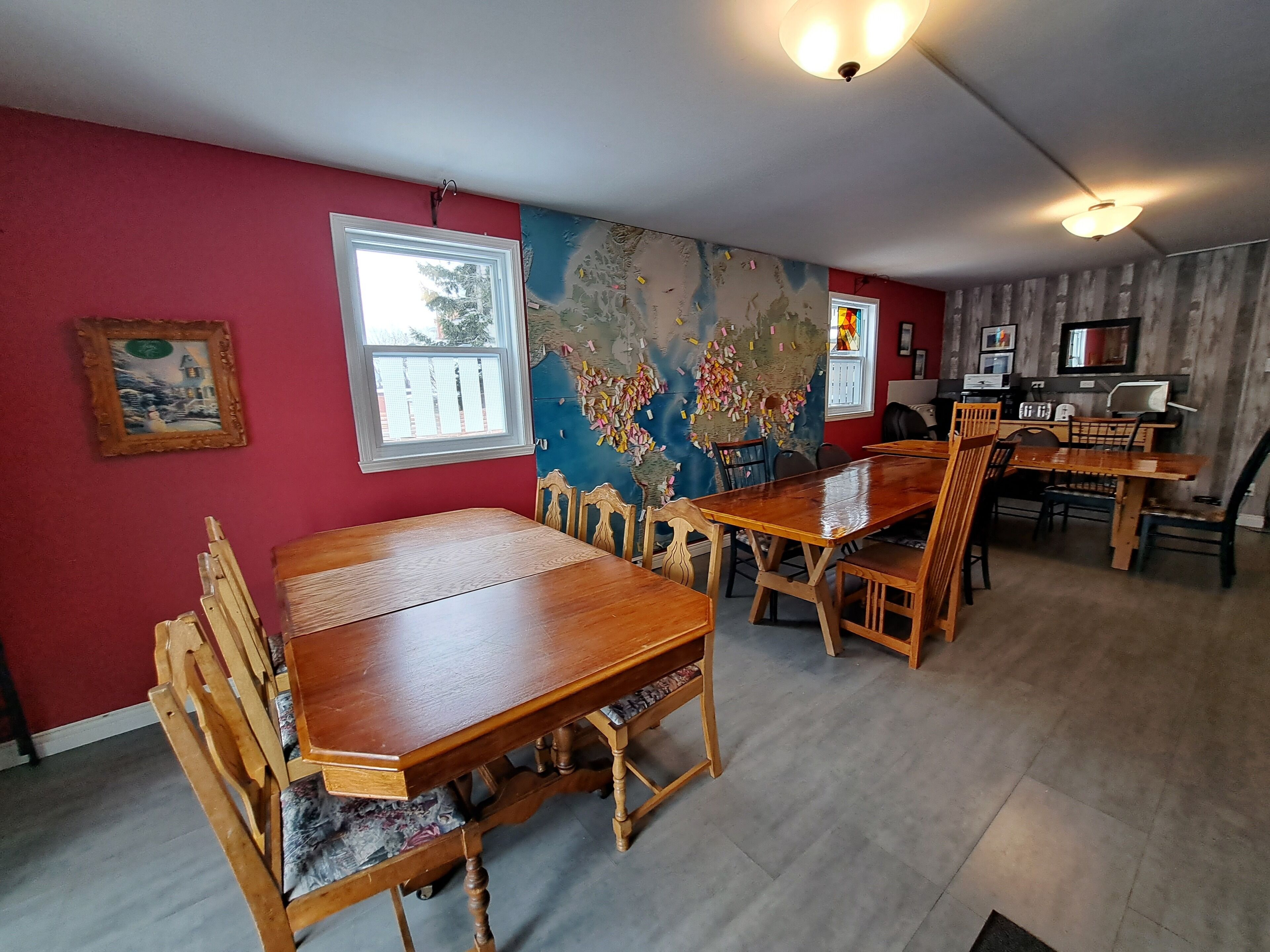 A dining area with wooden tables and chairs, a large world map on the wall, and a window with blinds.
