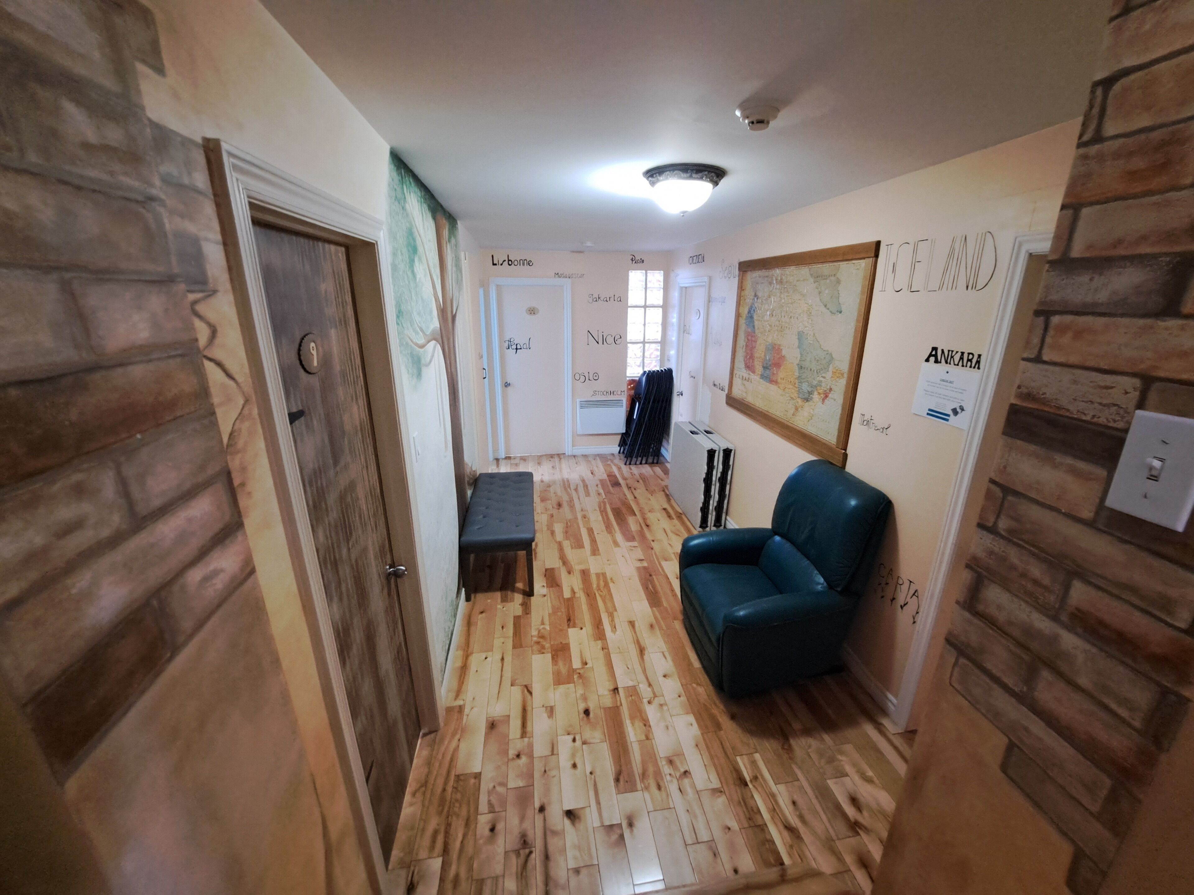 Un pasillo con suelo de madera, un banco, una silla azul y una pared con un mapa y texto.