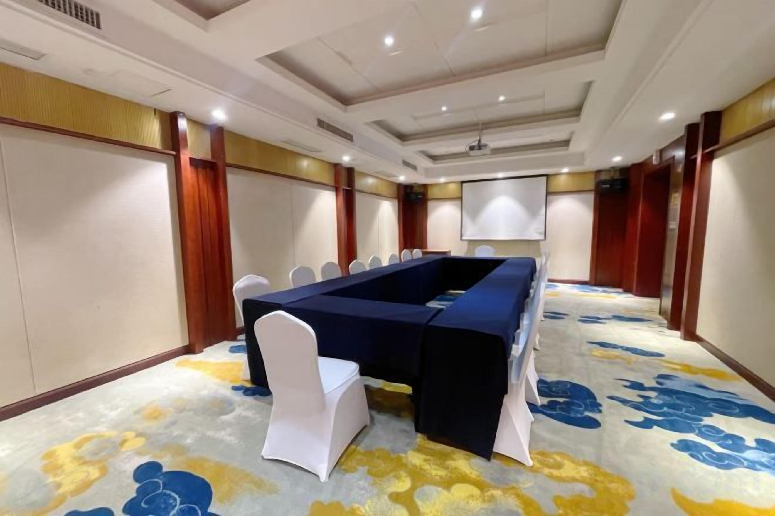 A conference room with a long table, white chairs, and a carpeted floor.