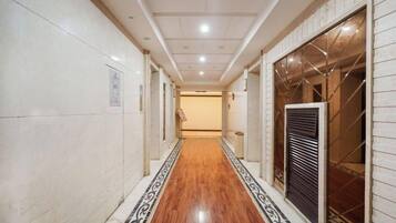 A corridor with a wooden floor and patterned border, leading to a room with a large window and a metal grille.