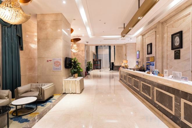A hotel lobby with a reception desk, seating area, and a large chandelier.