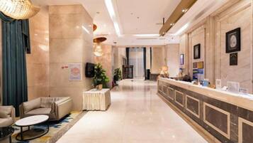 A hotel lobby with a reception desk, seating area, and a large chandelier.