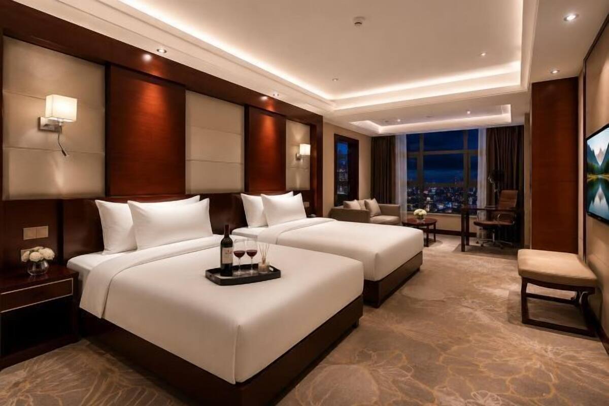 A hotel room with two beds, a seating area, a TV, and a city view.