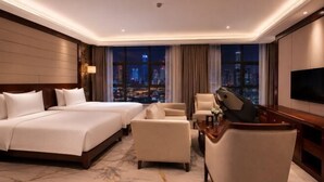 Une chambre d’hôtel avec un grand lit, deux fauteuils, un bureau, une télévision et une vue sur la ville.