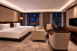 A hotel room with a large bed, two armchairs, a desk, a TV, and a city view. - Dingsheng International Hotel (Nanchang)
