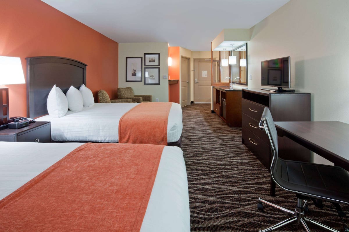 A hotel room with two beds, a desk, a chair, a television, and a bathroom.