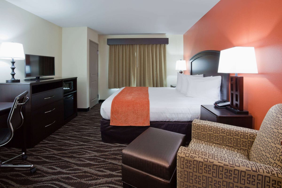 A hotel room with a bed, a desk with a TV, a chair, a sofa, and a lamp.