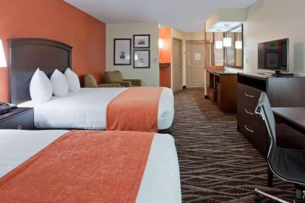Een hotelkamer met twee bedden, een bureau, een stoel, een televisie en een badkamer op de achtergrond.