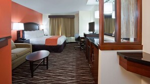 A hotel room with a bed, a desk, a chair, a sofa, and a mirror. - AmericInn by Wyndham Waupun (Waupun)