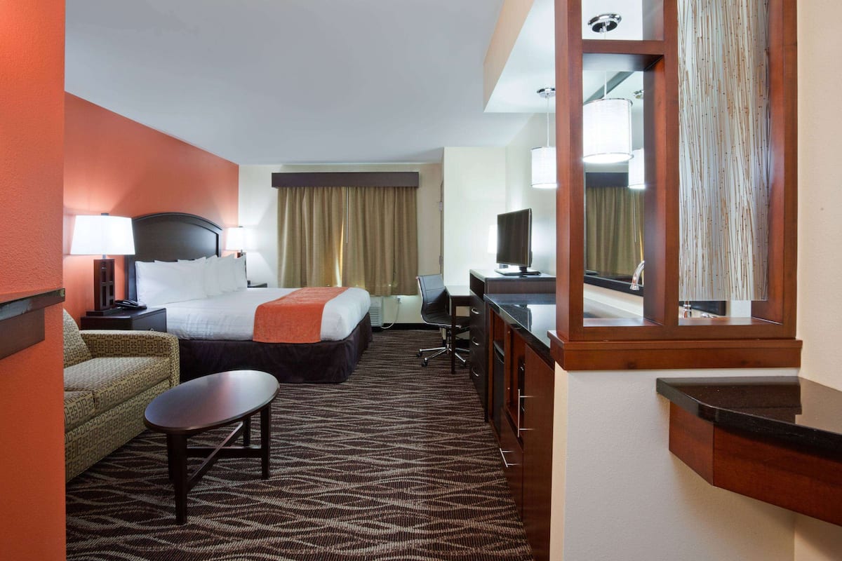 A hotel room with a bed, a desk, a chair, a sofa, and a mirror.