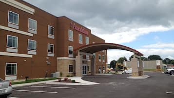 A hotel with a brown facade, a red arch entrance, and a parking lot.