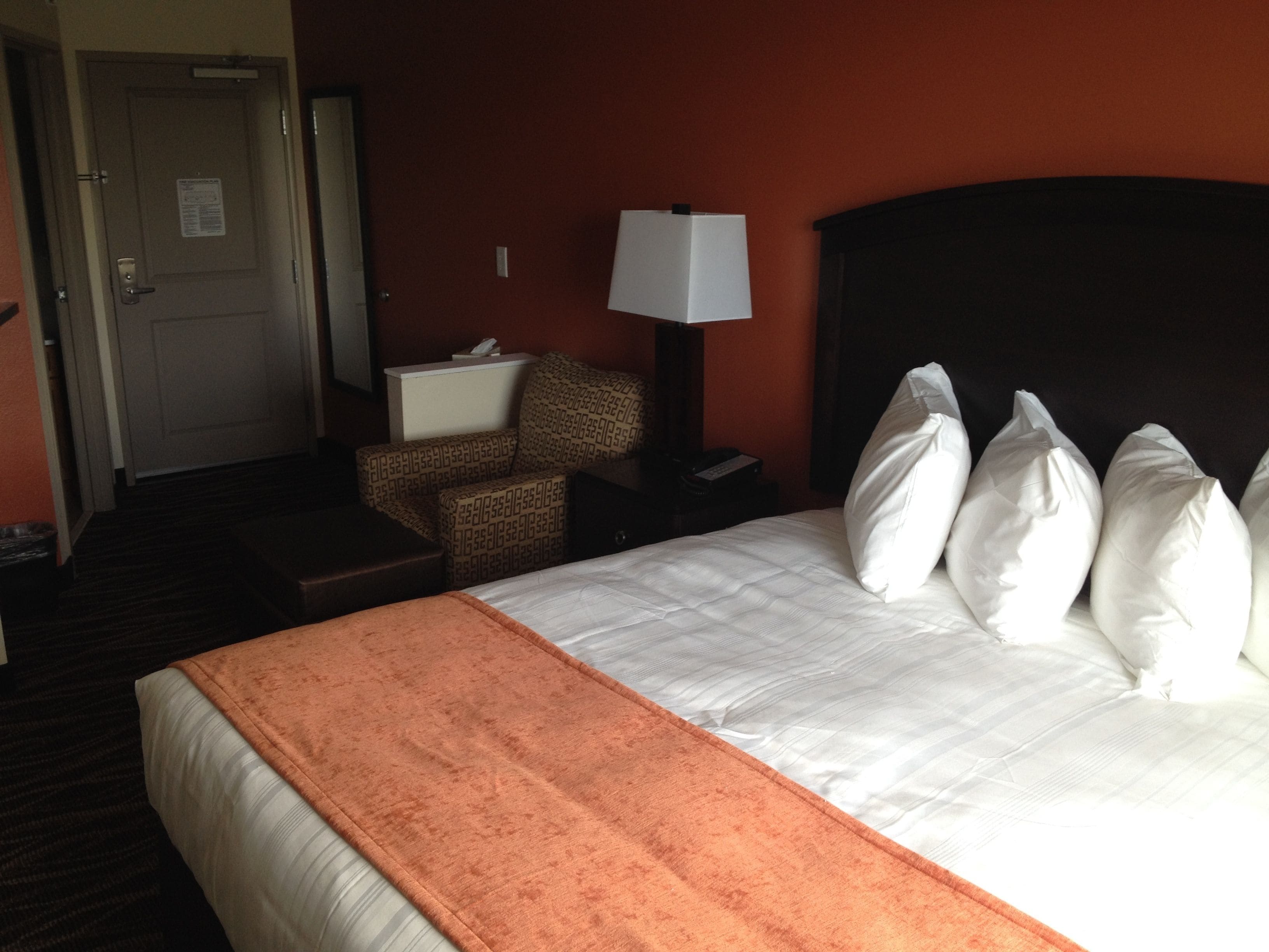 Une chambre d’hôtel avec un lit, une chaise, une table de chevet, une lampe et une porte.