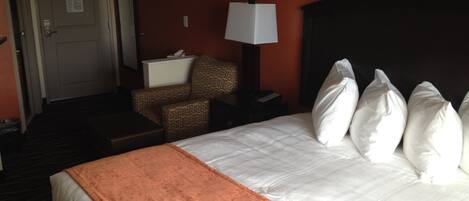 Une chambre d’hôtel avec un lit, une chaise, une table de chevet, une lampe et une porte.