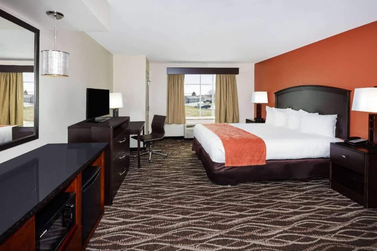 A hotel room with a bed, desk, TV, and a view of the outside.