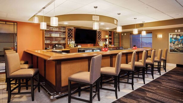 A bar area with a long counter, multiple chairs, and overhead lighting. - AmericInn by Wyndham Waupun (Waupun)