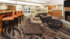 A hotel lobby with a reception desk, seating area with sofas and chairs, a fireplace, and a television mounted on the wall. - AmericInn by Wyndham Waupun (Waupun)