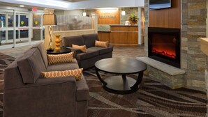 A lobby with a reception desk, a sofa set, a fireplace, and a TV mounted on the wall. - AmericInn by Wyndham Waupun (Waupun)