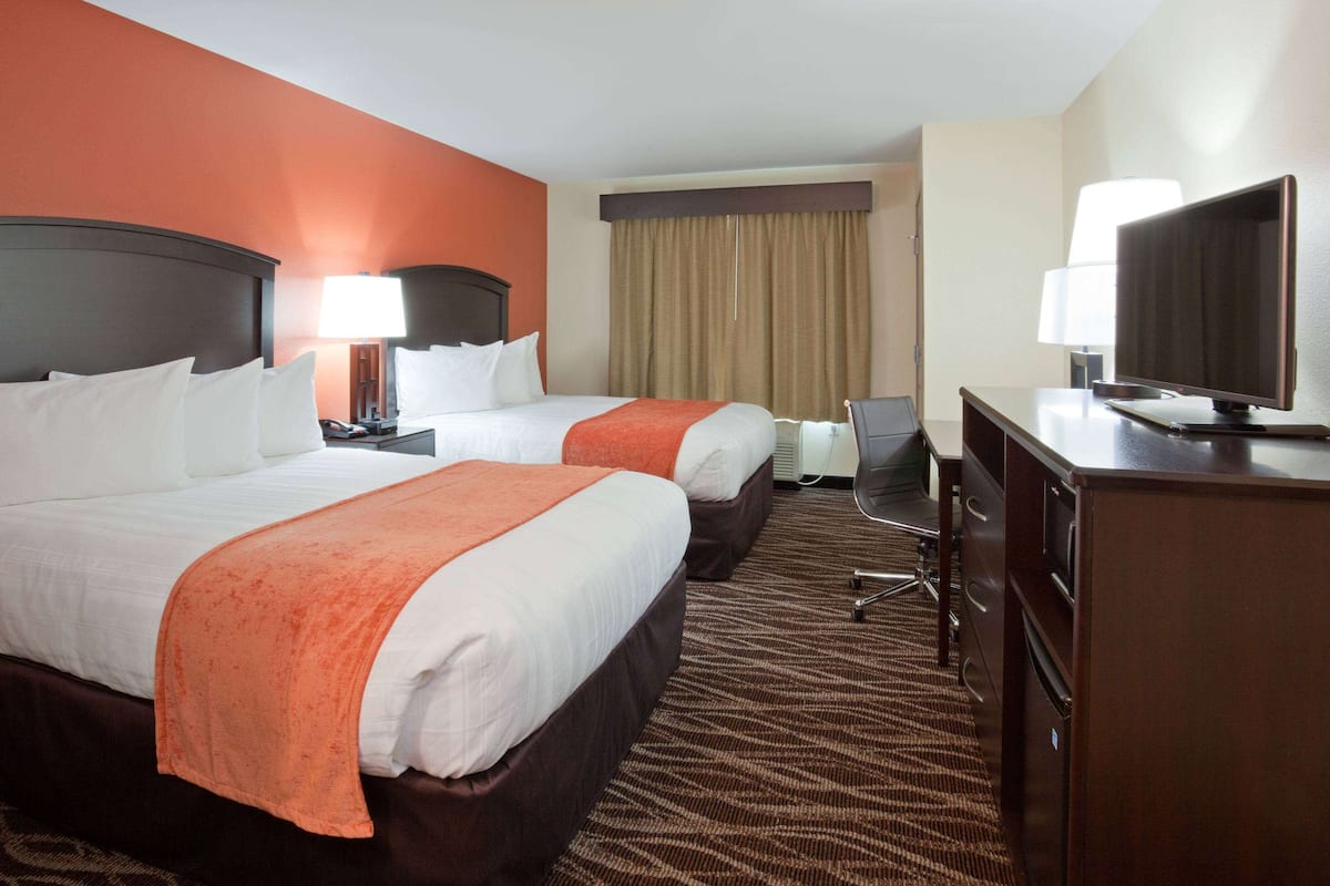 A hotel room with two beds, a desk, a television, and a desk lamp.