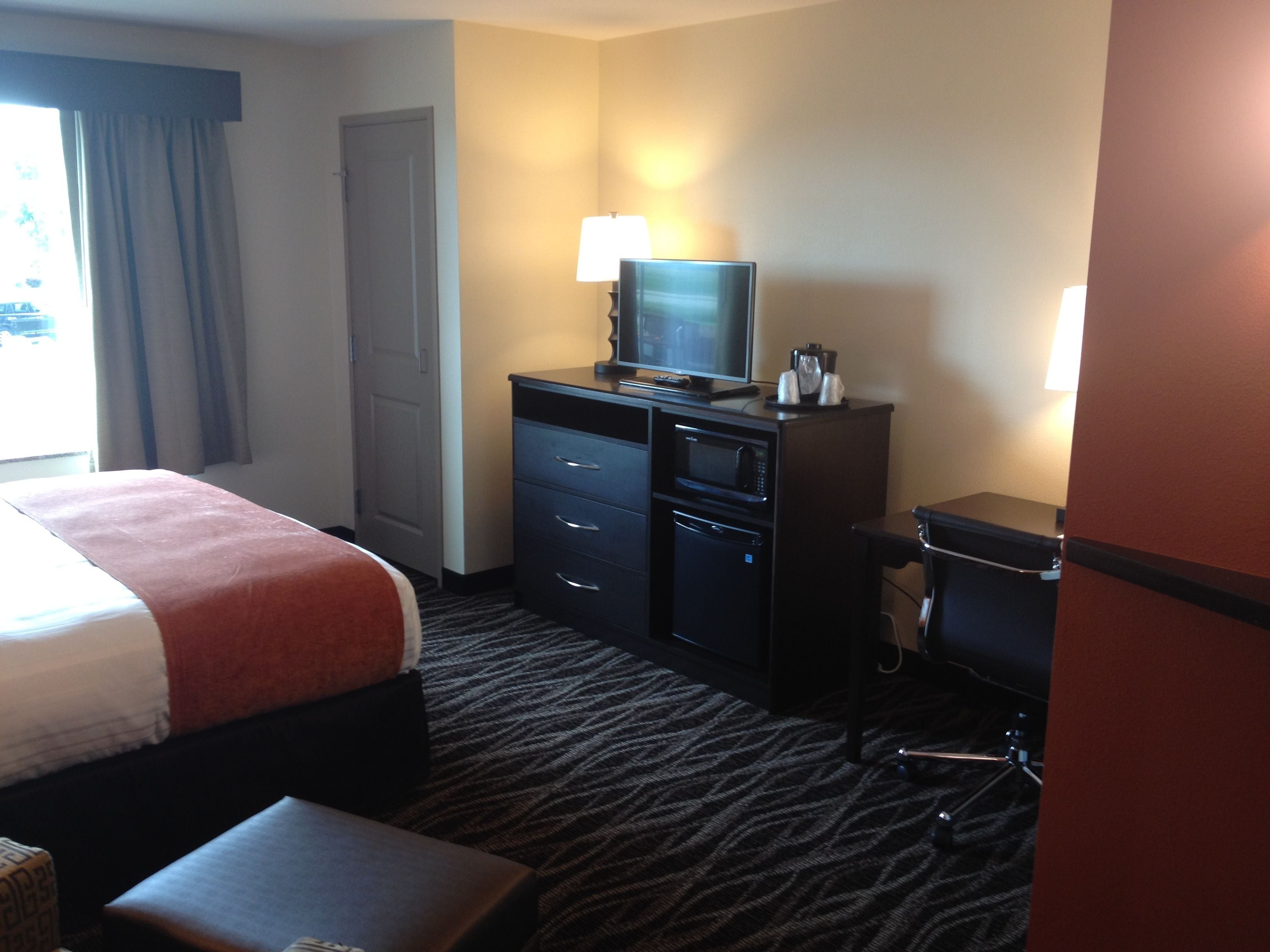 A hotel room with a bed, a desk with a computer, a microwave, and a coffee maker.