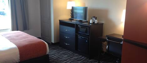Une chambre d’hôtel équipée d’un lit, d’un bureau avec un ordinateur, d’un four à micro-ondes et d’une machine à café.