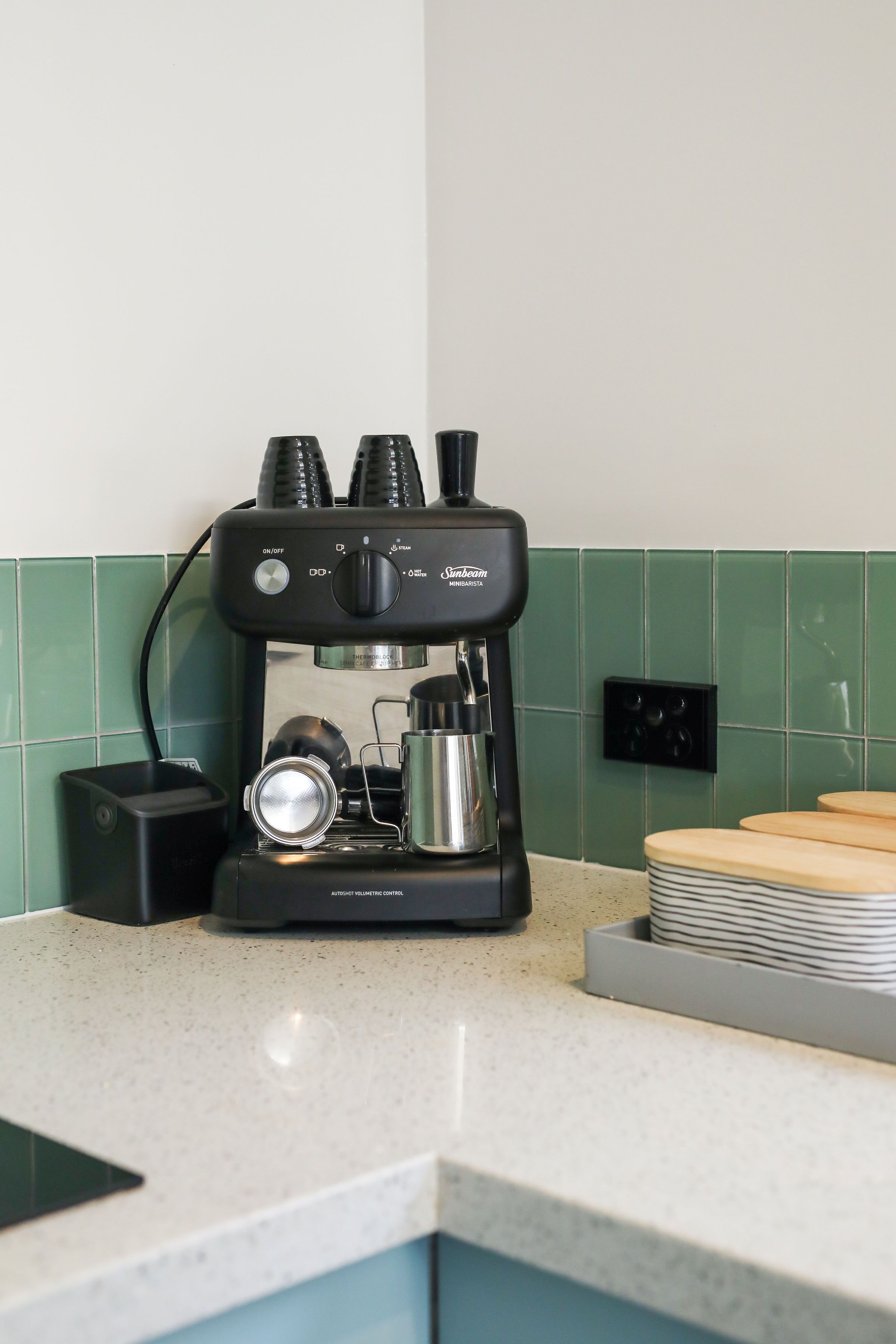 Een koffieapparaat op een aanrecht met een groene betegelde achterwand.