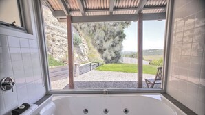 A bathroom with a large bathtub, a window with a view of a garden and a wooden fence. - Anchors Port Campbell (Port Campbell)