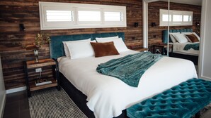 A bedroom with a wooden wall, a large bed with white bedding, a teal throw blanket, and a mirror. - Anchors Port Campbell (Port Campbell)