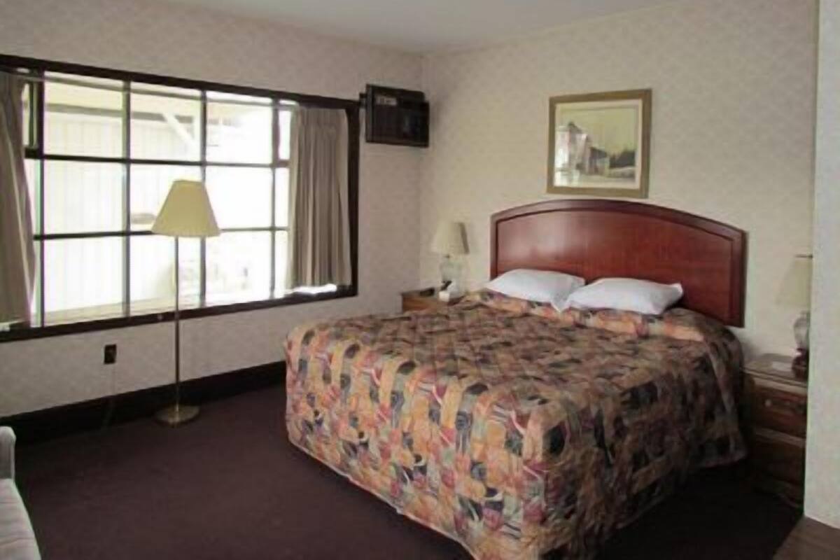 A hotel room with a large bed, a window with curtains, a wall-mounted TV, and a framed picture on the wall.