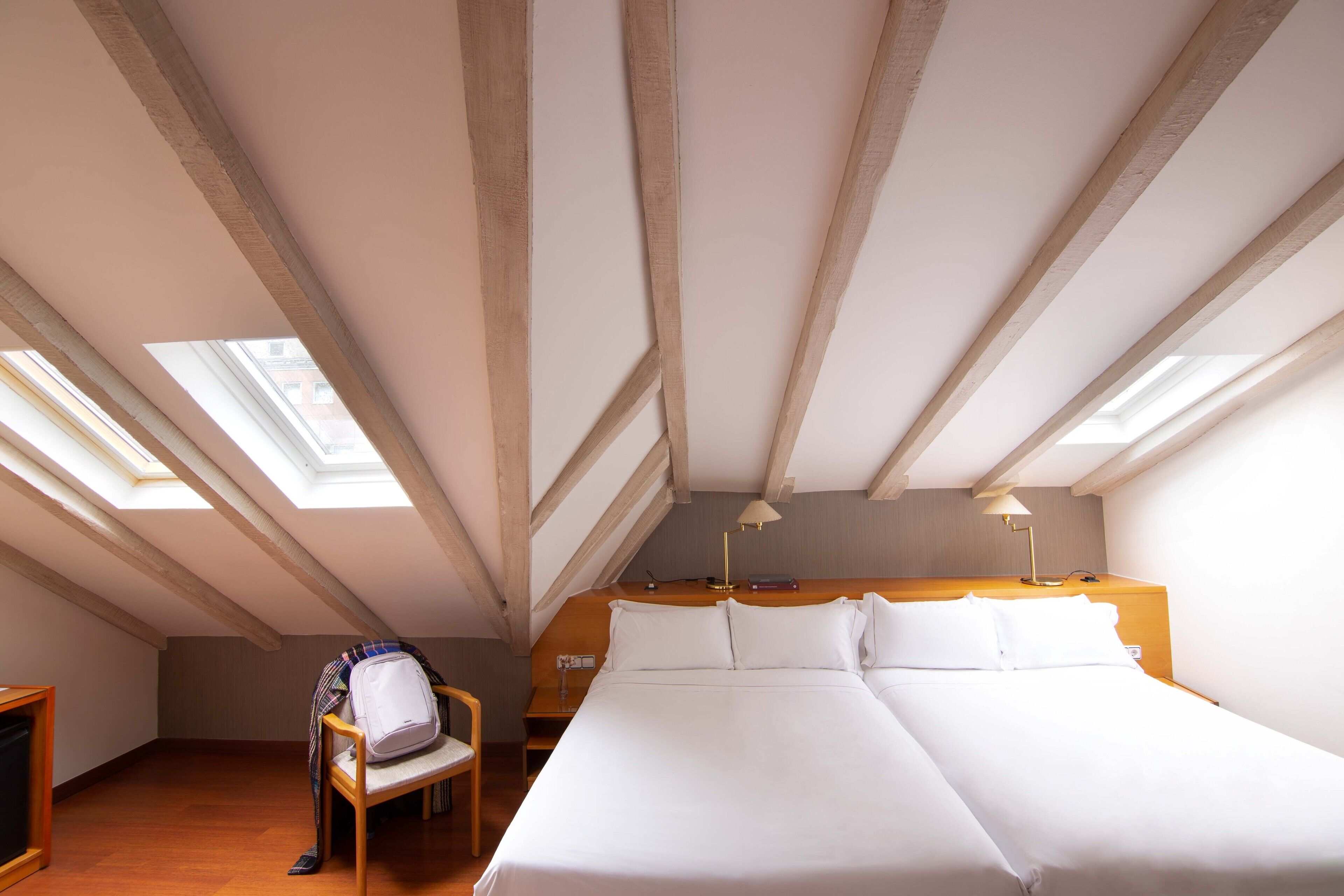A room with a large bed, skylights, a wooden headboard, and a bedside table with a lamp.