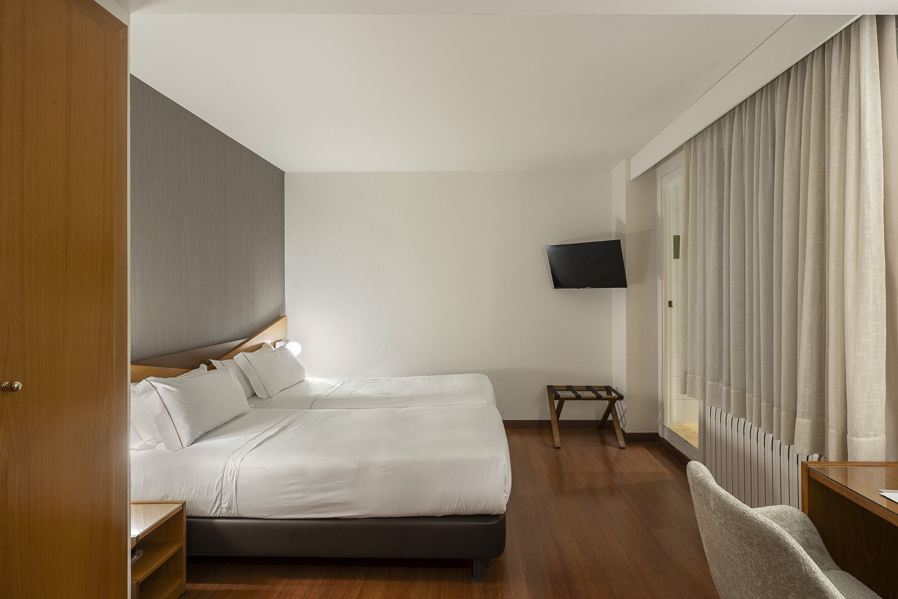 Une chambre d’hôtel avec un lit, un téléviseur fixé au mur, une petite table et une chaise.