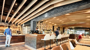 A modern bar area with wooden beams, a stone wall, and a counter with a computer. There are bar stools and tables with chairs. - Hotel de l'Isard (Andorra la Vella)