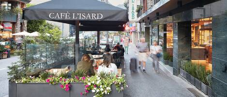 A cafe with outdoor seating, surrounded by urban buildings and greenery.