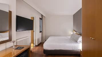 Habitación de hotel con cama, televisor en la pared, escritorio y silla, y un radiador.